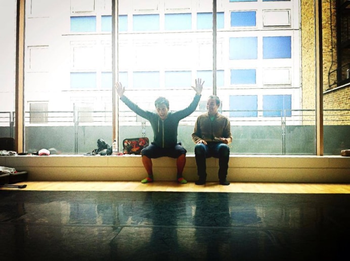 Two collaborators seated in front of a large rehearsal-studio window